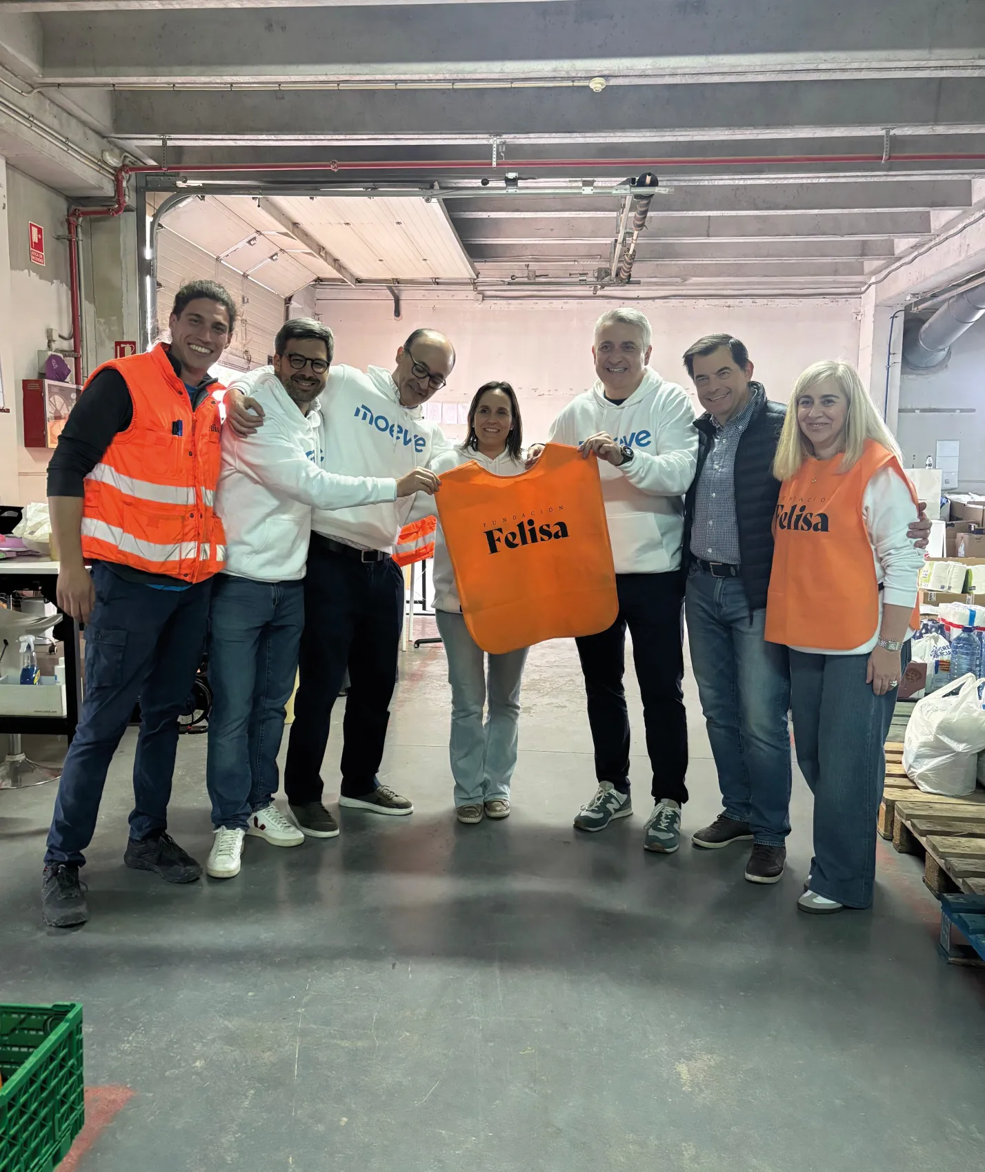Representantes de Moeve y Fundación Felisa posando con un chaleco de la fundación en una nave de donaciones