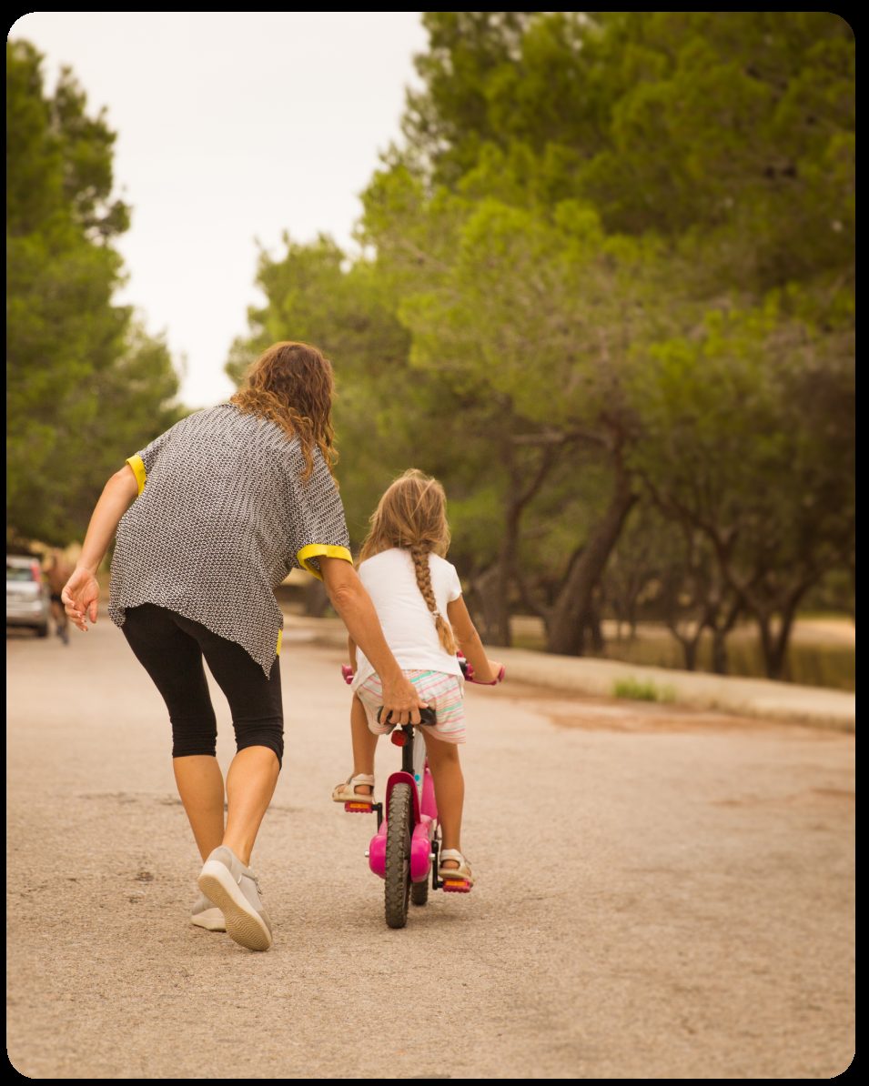 Una persona acompaña a una niña que aprende a montar en bici